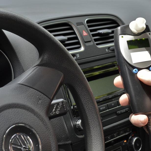 Im Cockpit eines Autos hält eine Hand ein Alkoholtestgerät.