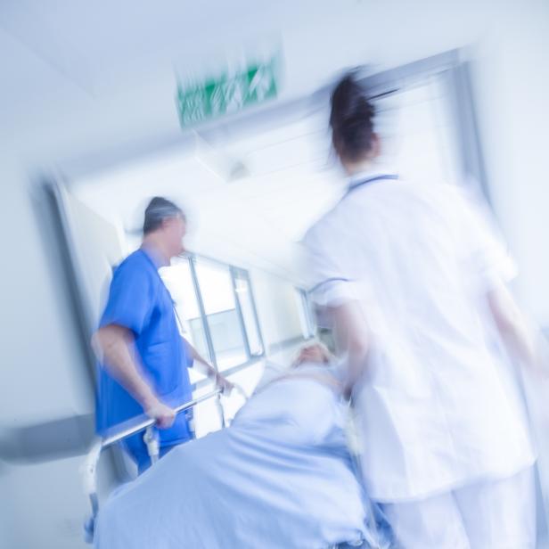 Zwei Pflegekräfte schieben eine Patientin auf einer Trage eilig durch einen Krankenhausflur.