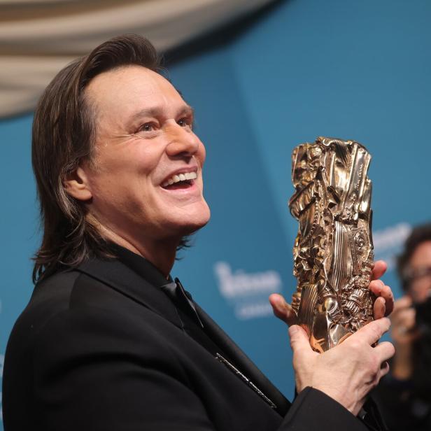 Ein lächelnder Jim Carrey bei den César Awards im Anzug hält eine goldene Trophäe in den Händen.