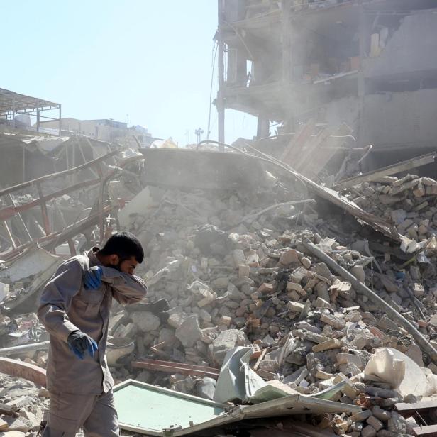 Ein Mann steht vor einem Trümmerhaufen, der von zerstörten Gebäuden stammt.