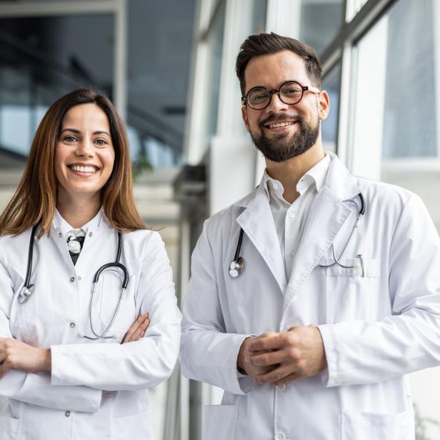 Two smiling doctors wearing white coats and stethoscopes in hospital corridor
