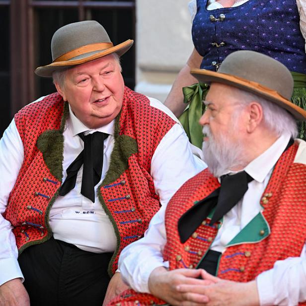 Wolfgang Schwalm and Wilfried Gliem in traditioneller Tracht unterhalten sich, eine Frau in Dirndl steht dahinter.