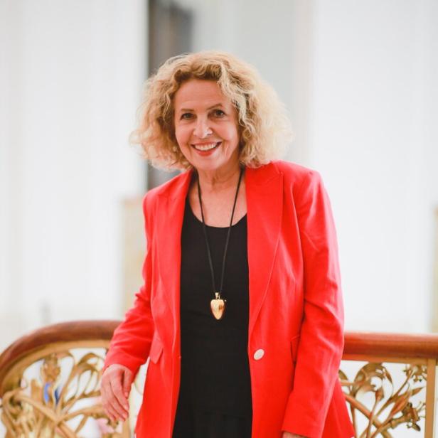 Eine lächelnde Michaela May mit blonden Locken trägt ein schwarzes Kleid und einen roten Blazer.