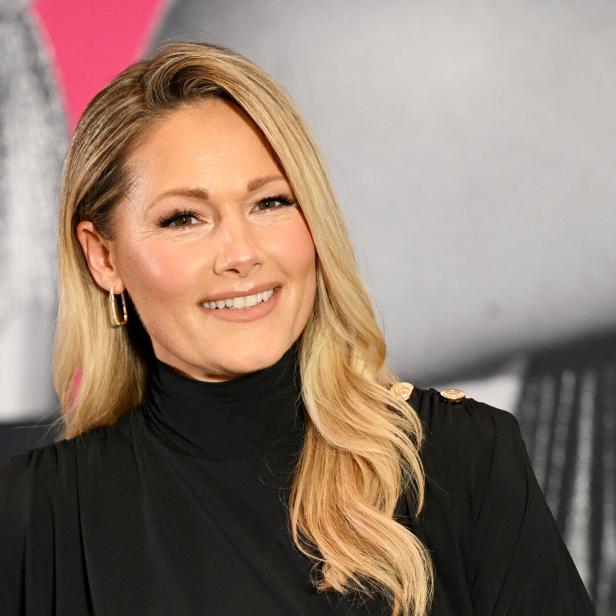 Helene Fischer lächelt mit blonden, gewellten Haaren und schwarzem Oberteil in die Kamera.