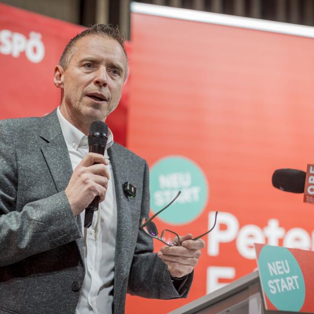 Ein Mann im grauen Sakko spricht an einem Rednerpult mit Mikrofon vor rotem Hintergrund mit SPÖ-Logos.