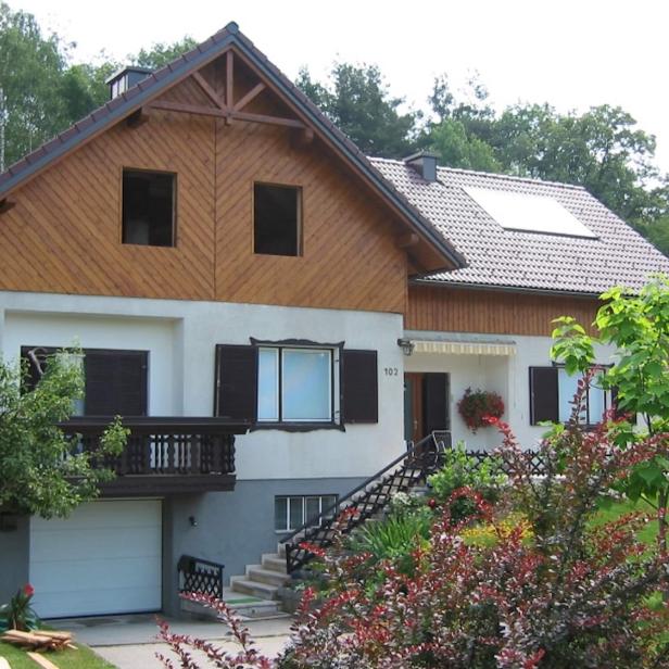Einfamilienhaus mit Holzfassade, Garten und umgeben von Bäumen an einem sonnigen Tag.