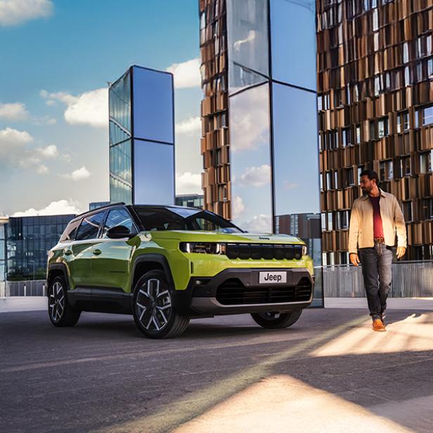 Der neue Jeep Compass steht vor einem Gebäude geparkt, daneben geht ein Mann.