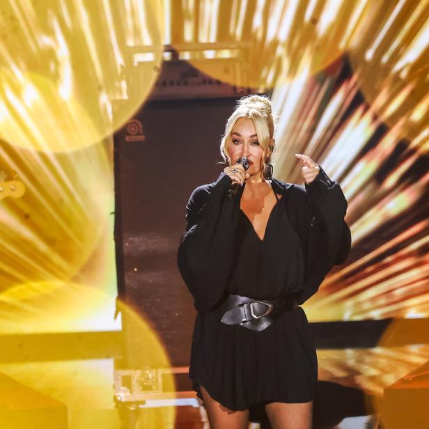 Sarah Connor performt in einem schwarzen Kleid mit Gürtel vor einem gelben Bühnenhintergrund.