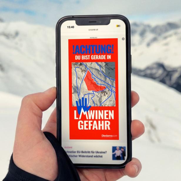 Eine Hand hält ein Smartphone, das eine Lawinengefahr-Warnung für Diedamskopf anzeigt.