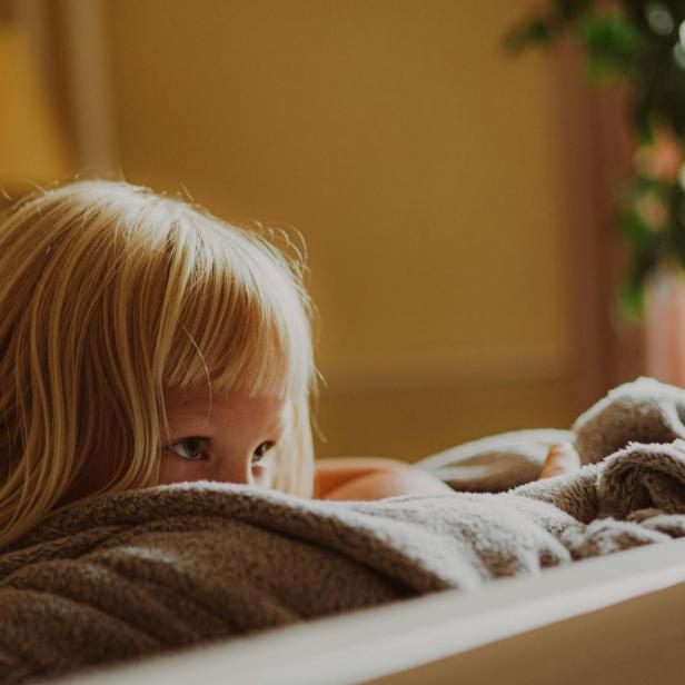 Ein blondes Mädchen liegt nachdenklich auf einem Bett und blickt zur Seite.
