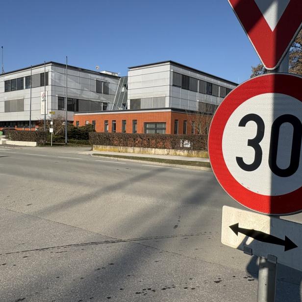 Ein 30 km/h-Schild steht am Straßenrand vor einem modernen Bürogebäude.
