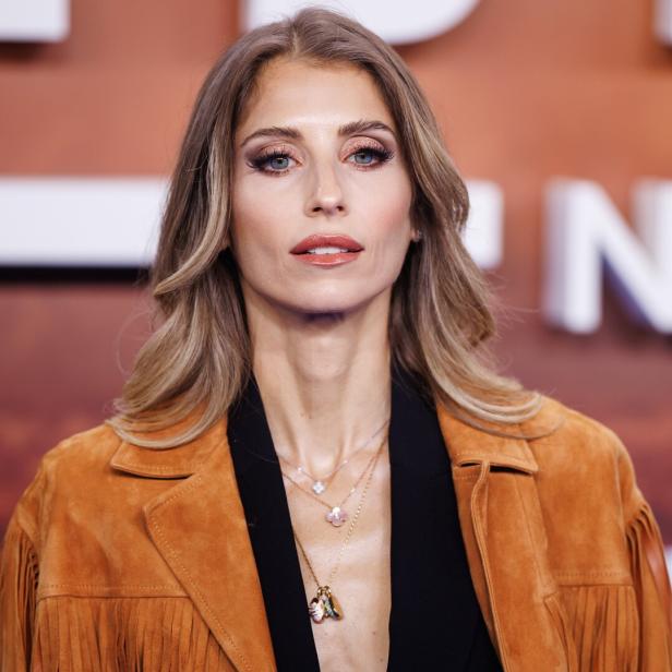 Cathy Hummels mit blonden Haaren und brauner Jacke mit Fransen blickt in die Kamera.