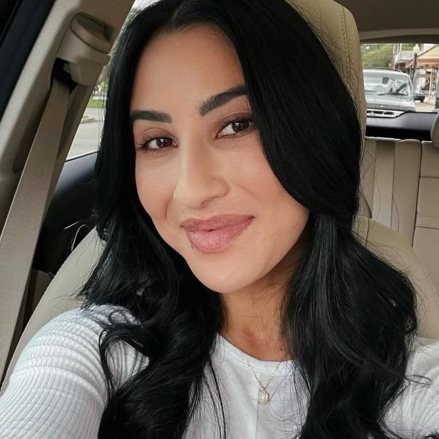 Frau mit langen dunklen Haaren lächelt auf dem Beifahrersitz eines Autos in die Kamera.