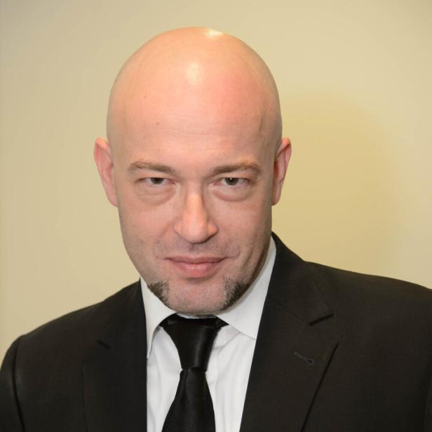 Der Graf mit Glatze und im schwarzen Anzug mit weißem Hemd und schwarzer Krawatte schaut direkt nach vorn.