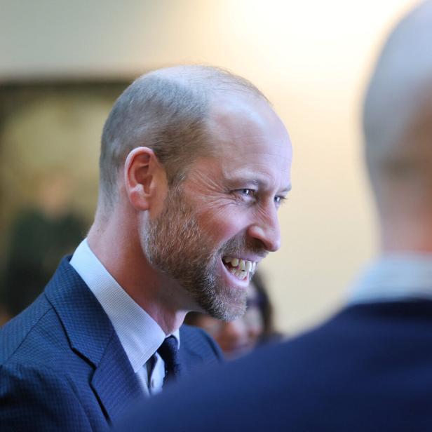 Prinz William lächelt in einem dunklen Anzug, während er sich mit jemandem unterhält.