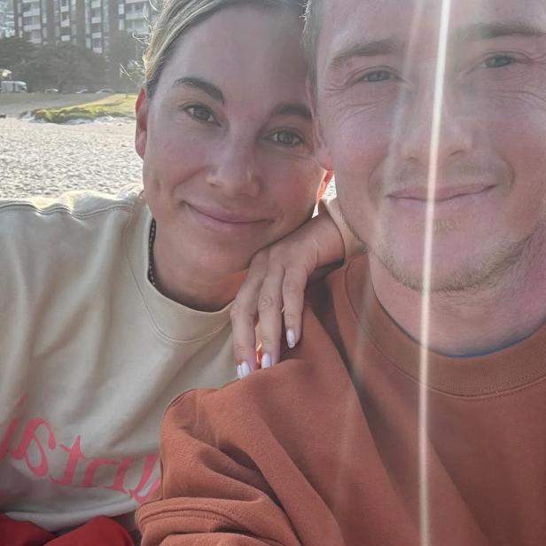 Pärchen sitzt am Strand und lächelt in die Kamera