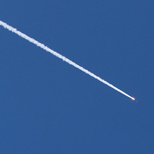 Eine Rakete zieht eine weiße Rauchspur durch den blauen Himmel.
