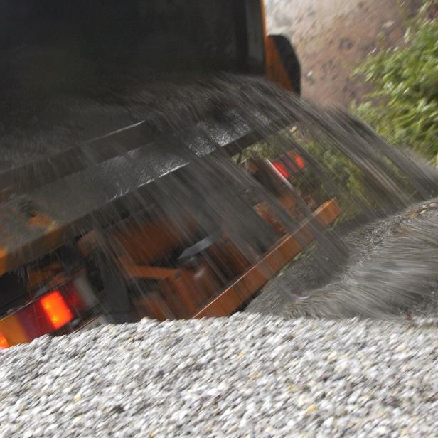 Ein Lastwagen kippt eine große Menge Kies auf einen Haufen neben einigen grünen Ästen ab.