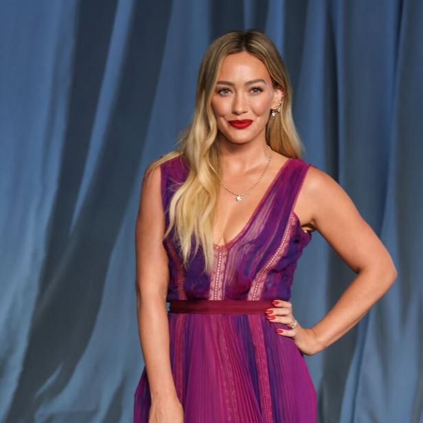 Hilary Duff trägt ein langes, violettes Kleid mit roten Lippen.