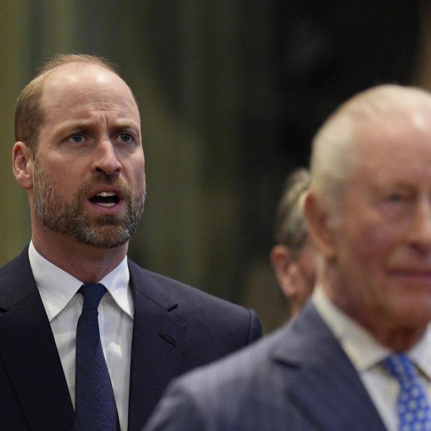Prinz William im Hintergrund, König Charles im Vordergrund. Beide tragen Anzüge und schauen ernst.