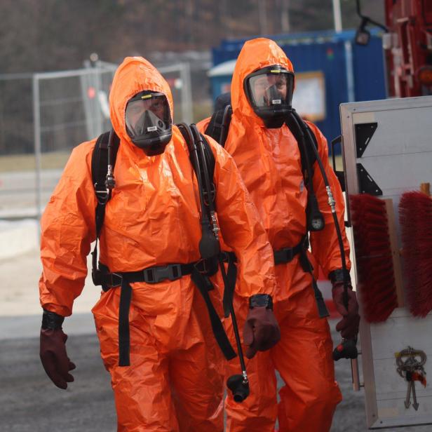 Zwei Personen in orangen Schutzanzügen mit Schutzmasken