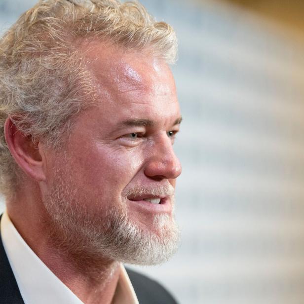 Eric Dane mit grauem Haar und Bart, gekleidet in einem dunklen Anzug, blickt nach rechts. 