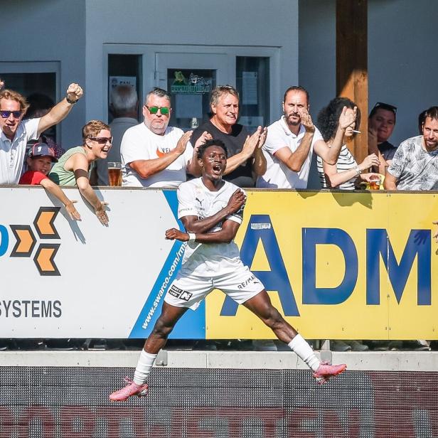 Ein Fußballspieler (Alieu Conateh) jubelt vor begeisterten Fans, die am Spielfeldrand klatschen und jubeln.