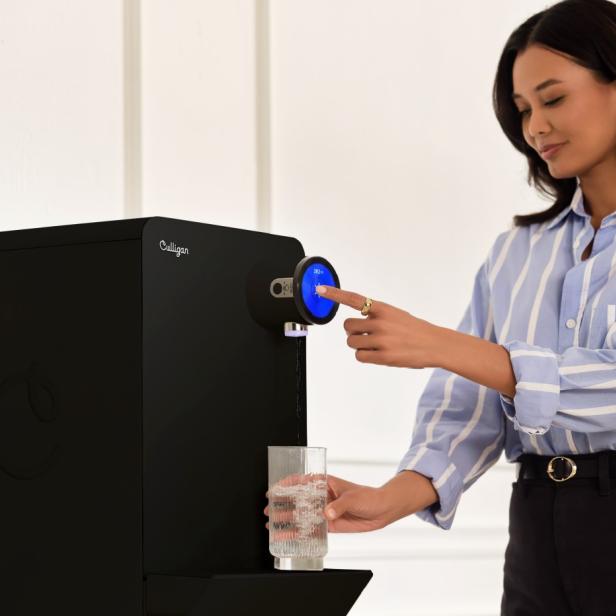 Eine Frau füllt ein Wasserglas an einem Wasserspender auf.