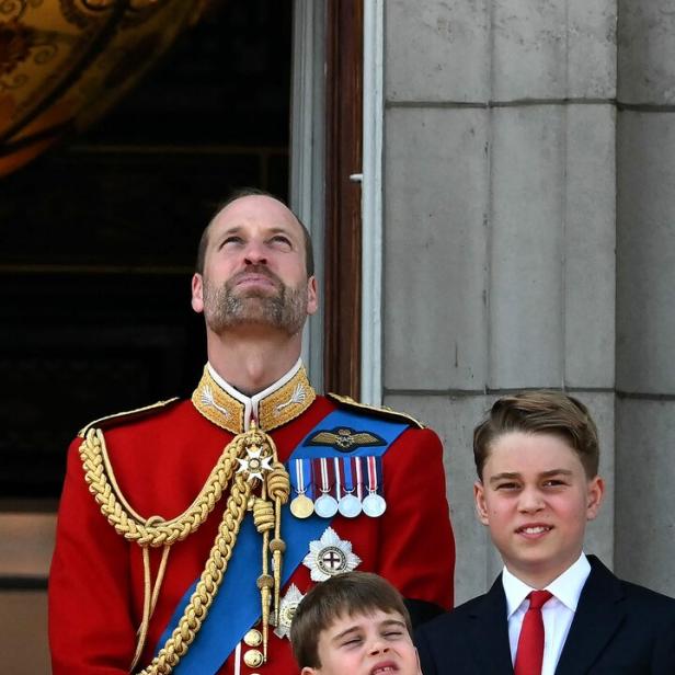 Prinz William steht mit seinen Söhnen George und Louis auf einem Balkon und schaut nach oben.