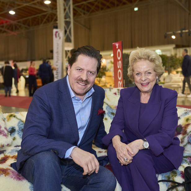 Zwei Personen sitzen auf einem Sofa mit Blumenmuster in einer Halle.