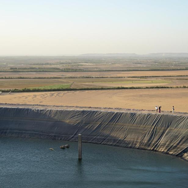 Großer künstlicher Wasserspeicher am Rand einer Wüstenlandschaft mit mehreren Personen am Beckenrand.