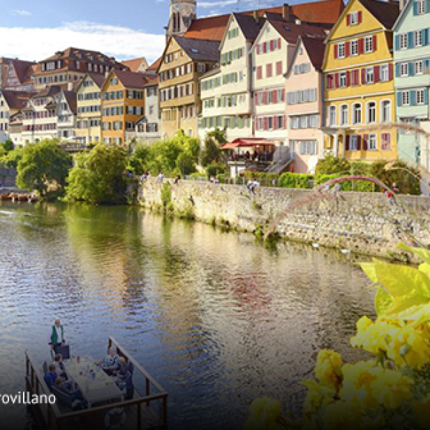 Bunte Fachwerkhäuser am Flussufer mit Stocherkahn und Blumen im Vordergrund.