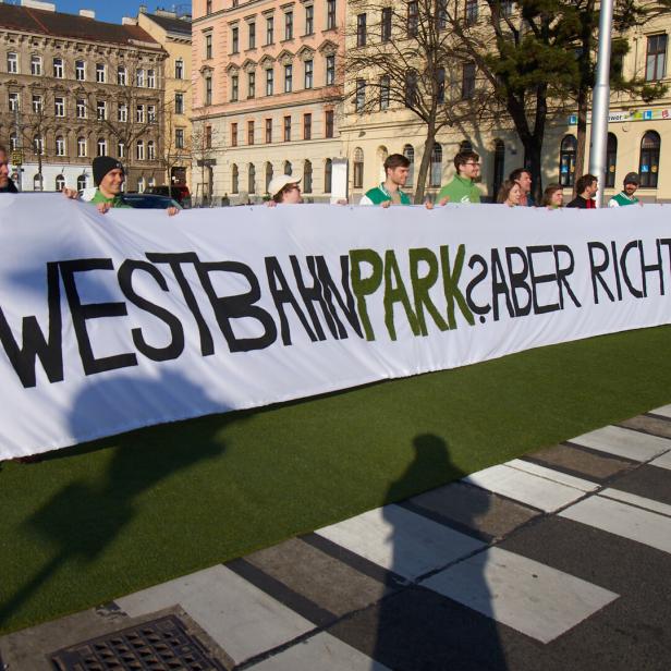 Mehrere Menschen halten ein langes Transparent mit der Aufschrift „WESTBAHNPARK? ABER RICHTIG!“ auf einer Straße.