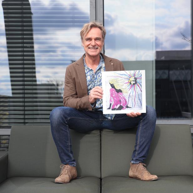 Ein Mann sitzt auf einem Sofa und hält ein Bild mit einer farbenfrohen Illustration.