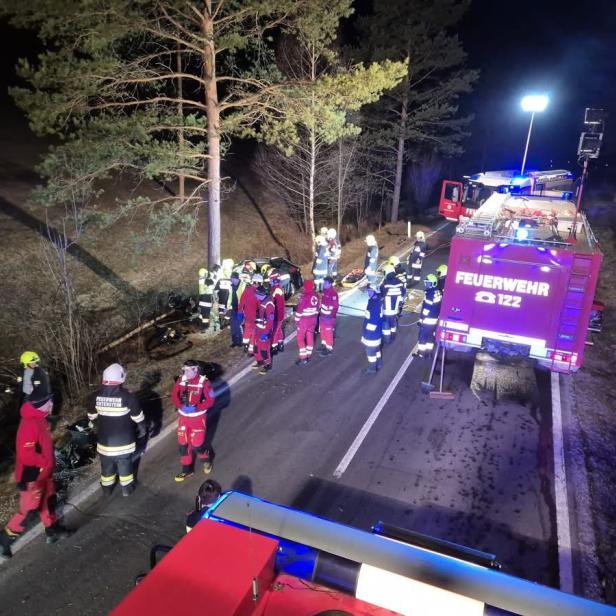 Ein Foto von dem Feuerwehreinsatz von oben. Mehrere Personen und Feuerwehrautos stehen nachts auf dem Straße neben dem Unfallfahrzeug.