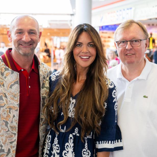 Drei Personen lächeln gemeinsam in einem Einkaufszentrum in die Kamera.