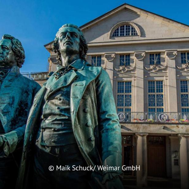 Goethe- und Schiller-Denkmal vor dem Deutschen Nationaltheater in Weimar bei blauem Himmel.