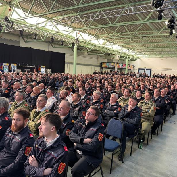 Viele Feuerwehrleute in Uniform sitzen dicht gedrängt in einer großen Halle und hören aufmerksam zu.