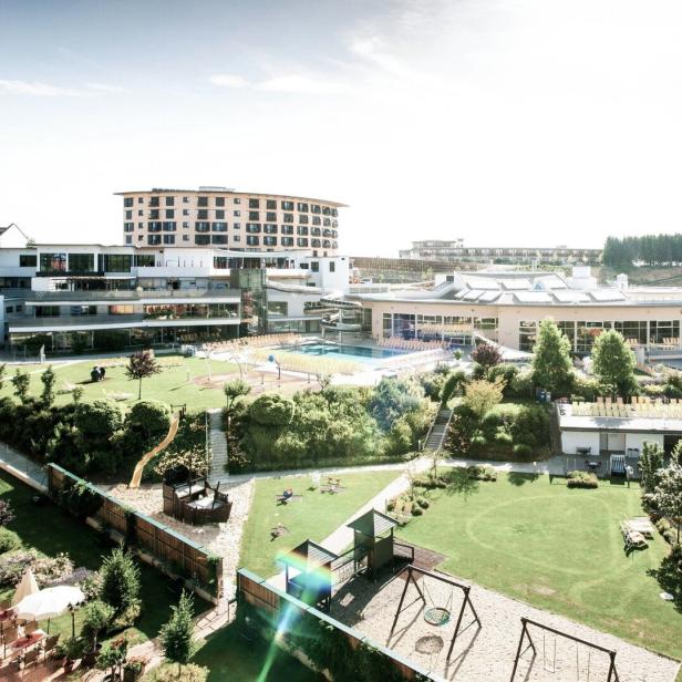 Große Hotelanlage mit mehreren Gebäuden, Außenpool, Spielplatz und weitläufigen Grünflächen bei sonnigem Wetter.