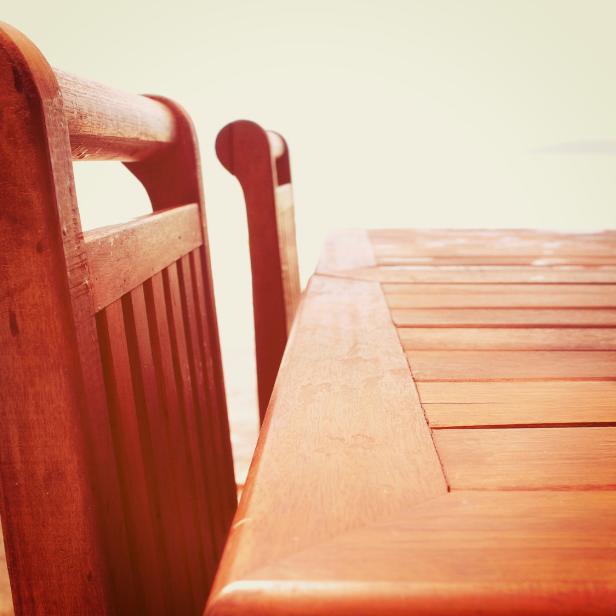 Holztisch und zwei Holzstühle mit Blick auf einen hellen, unscharfen Hintergrund.