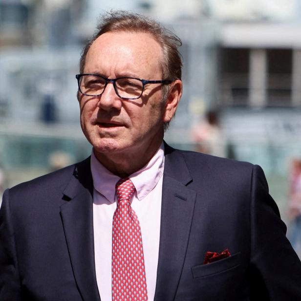 Kevin Spacey mit Brille, Anzug und roter Krawatte blickt in die Ferne.