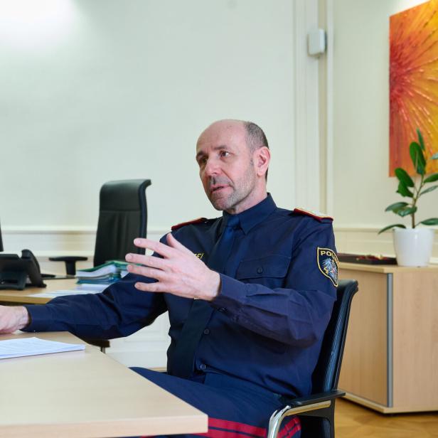 Ein Polizist in Uniform sitzt an einem Schreibtisch und gestikuliert während eines Gesprächs.