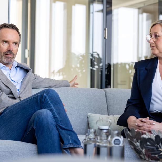 Zwei Personen sitzen auf einem Sofa und führen ein Gespräch in einem modernen Büro mit Glaswänden.