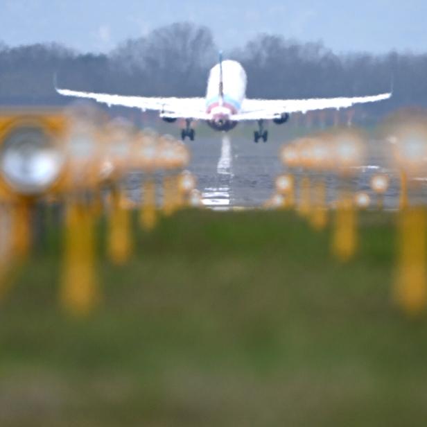 Ein Flugzeug hebt von einer Landebahn ab, umgeben von gelben Landebahnlichtern und unscharfem Hintergrund.