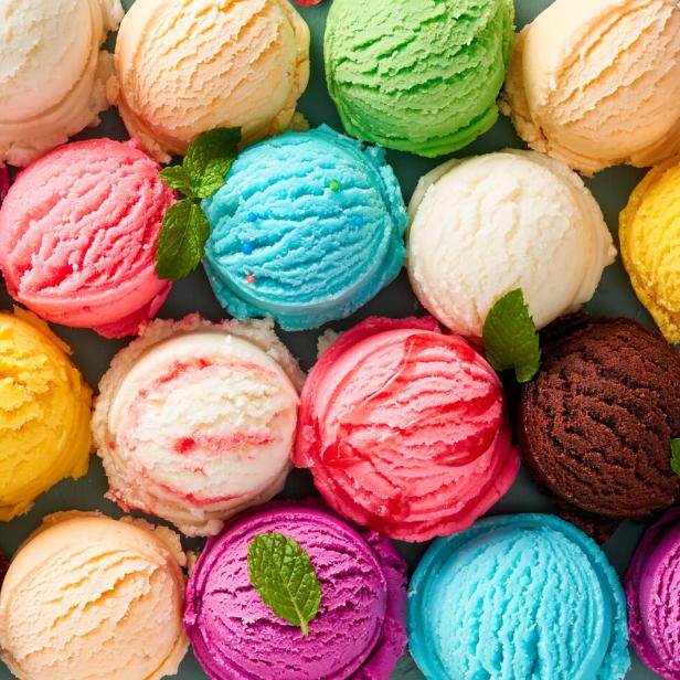 Viele bunte Eiskugeln in verschiedenen Geschmacksrichtungen, einige mit Minzblättern garniert, liegen dicht nebeneinander.