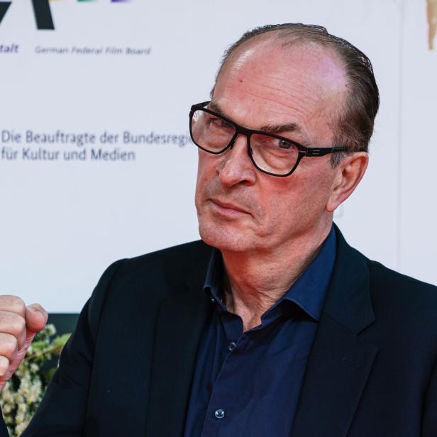 Ein Mann mit Brille und ernstem Gesichtsausdruck hebt die Faust, trägt dunkles Sakko und Hemd.