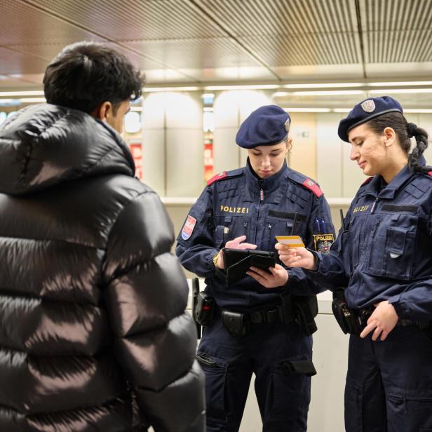 Zwei Polizistinnen kontrollieren die Ausweisdokumente eines Mannes in einer Bahnhofshalle.