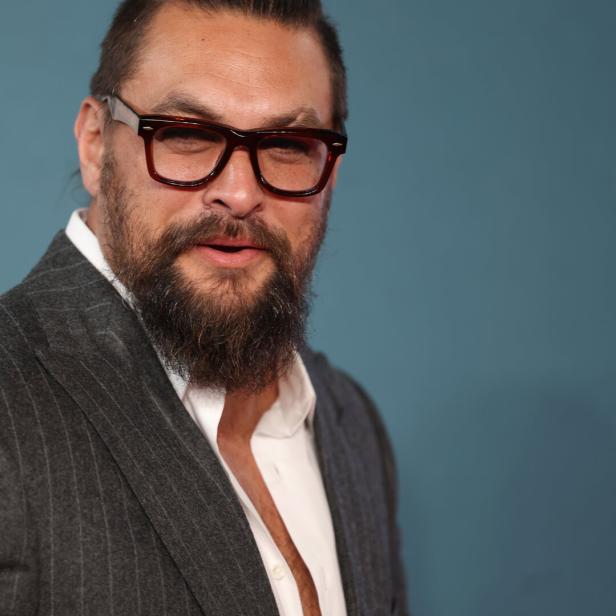 Jason Momoa mit Bart und Brille trägt einen grauen Anzug.