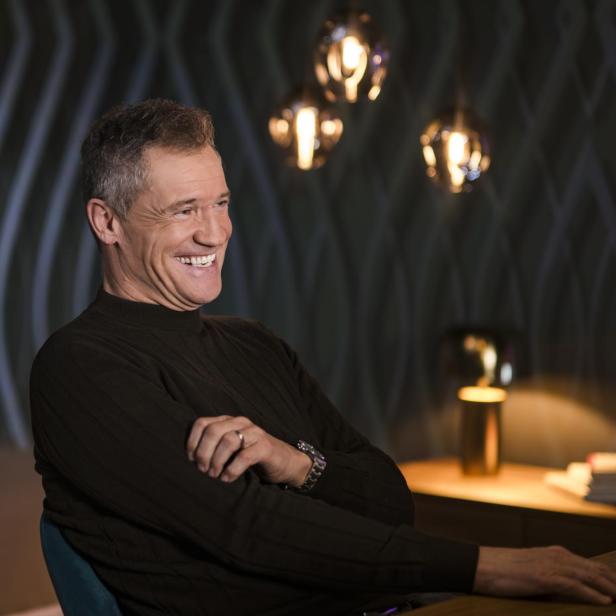 Armin Assinger in einem schwarzen Pullover, lachend