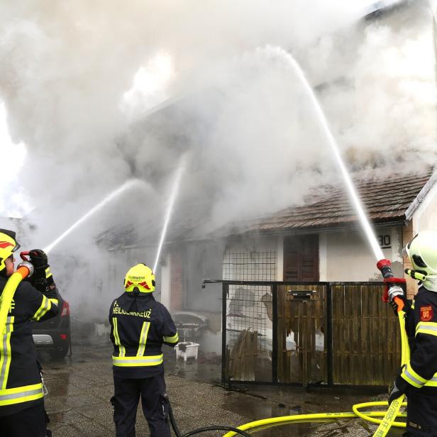 Drei Feuerwehrleute löschen mit Wasserschläuchen ein brennendes, stark verrauchtes Wohnhaus.